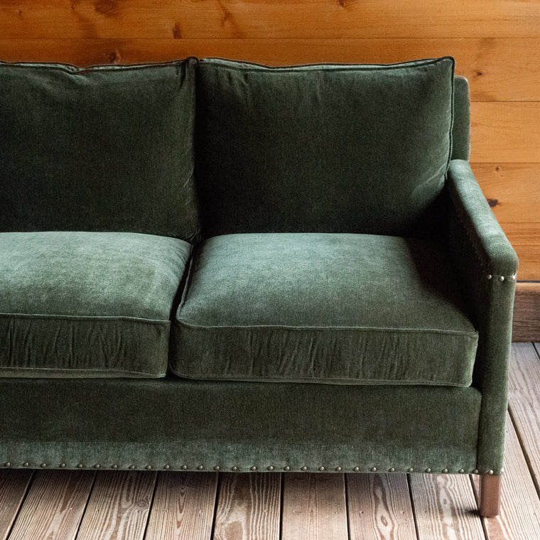 Three seat, loose back cushion sofa upholstered in green velvet with track arms and nailhead trim, back view