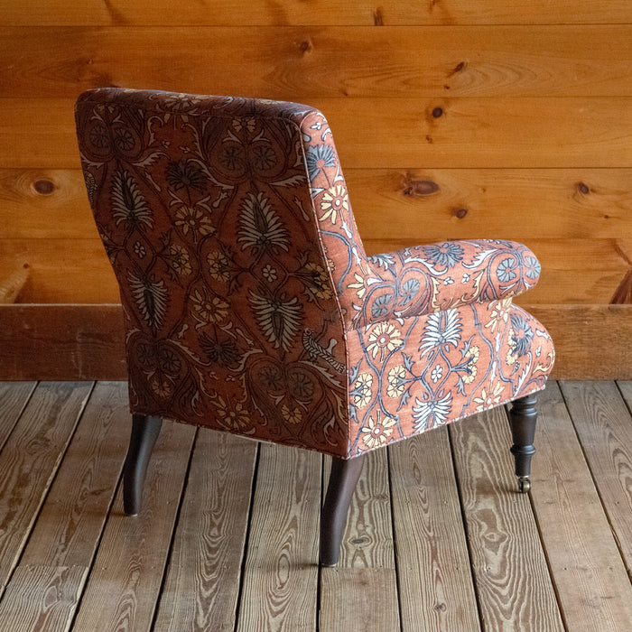 Tight seat and back chair upholstered in a floral block print fabric with pleated roll arms and turned front legs on casters, Angled back view