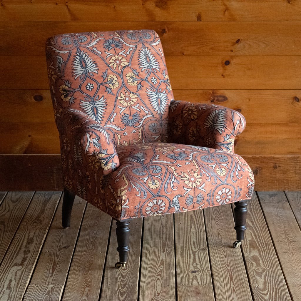 Tight seat and back chair upholstered in a floral block print fabric with pleated roll arms and turned front legs on casters, Angled front view