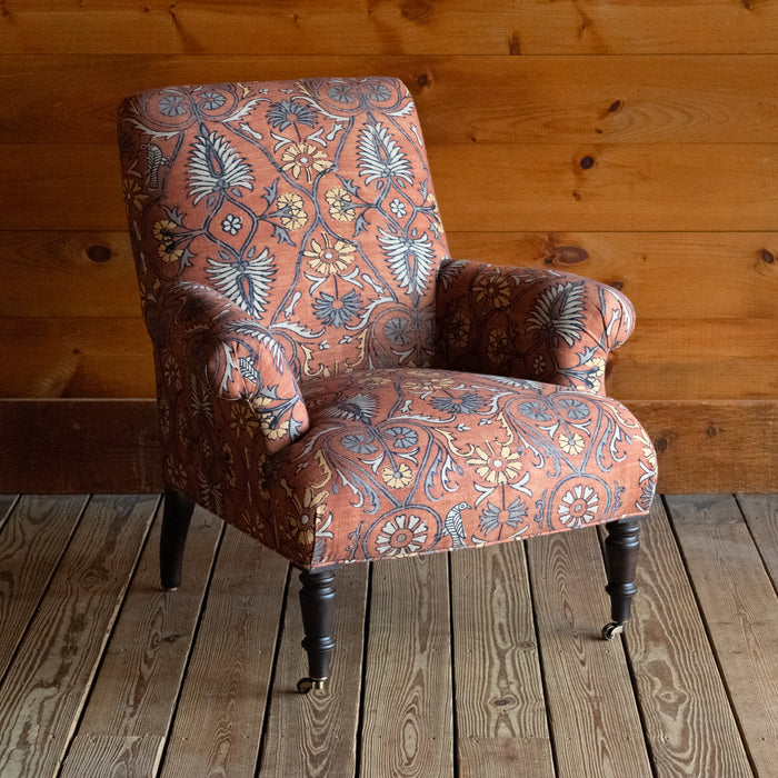 Tight seat and back chair upholstered in a floral block print fabric with pleated roll arms and turned front legs on casters, Angled front view