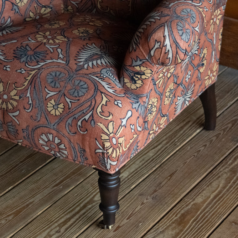 Tight seat and back chair upholstered in a floral block print fabric with pleated roll arms and turned front legs on casters, Fabric detail