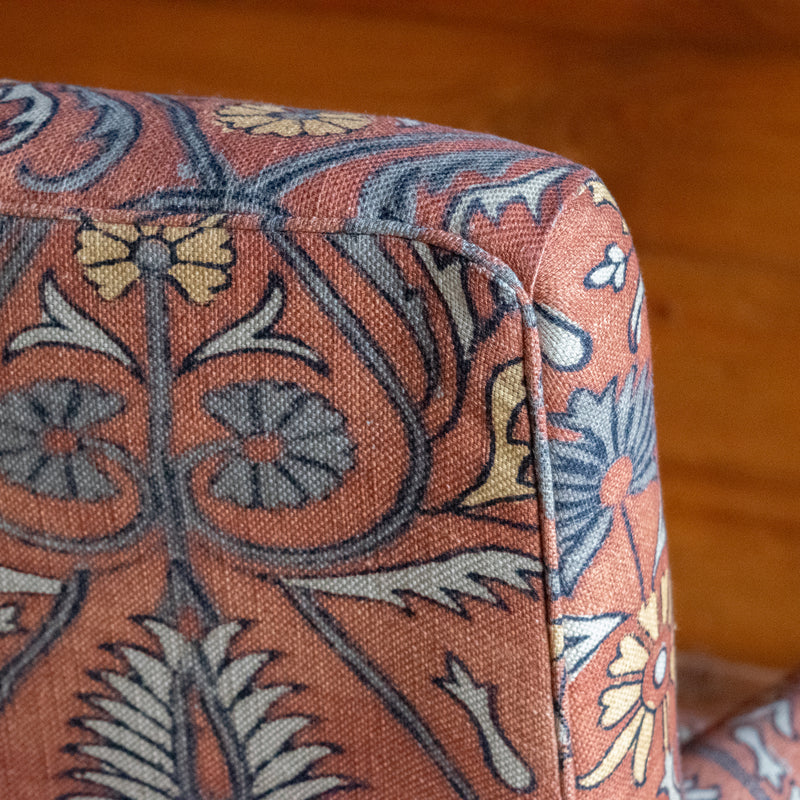 Tight seat and back chair upholstered in a floral block print fabric with pleated roll arms and turned front legs on casters, Mini welt trim detail