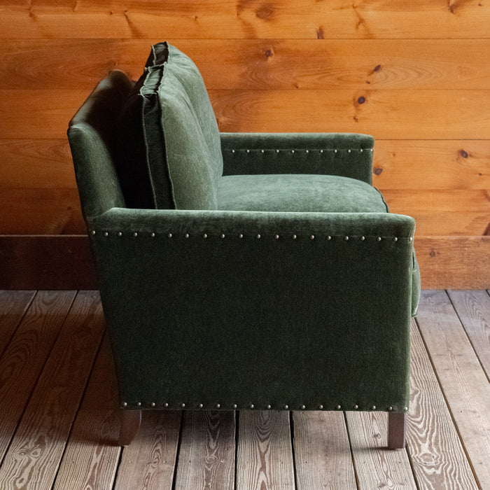 Loose back loveseat upholstered in a green velvet fabric with track arms and nailhead trim, Profile view